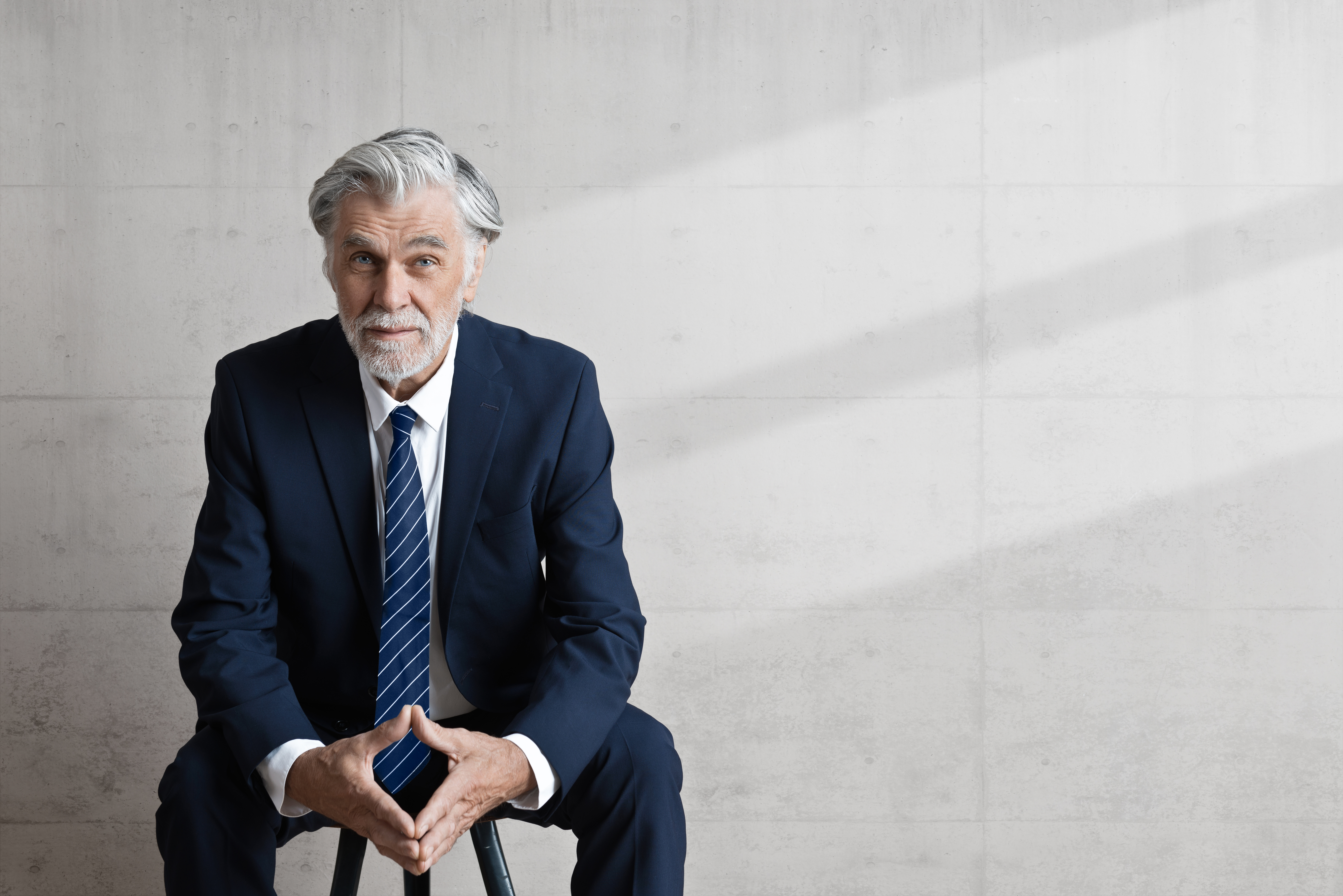 Sitzender, souveräner seniorer Business Mann in blauen Anzug und in modernem Gebäude von top Headhunter Schweiz, Bornhauser People's Management AG 