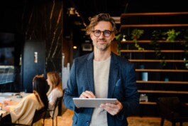 Zufriedener Personalberater SAP steht im Büro mit einem iPad in der Hand und sieht lächelnd in die Kamera 