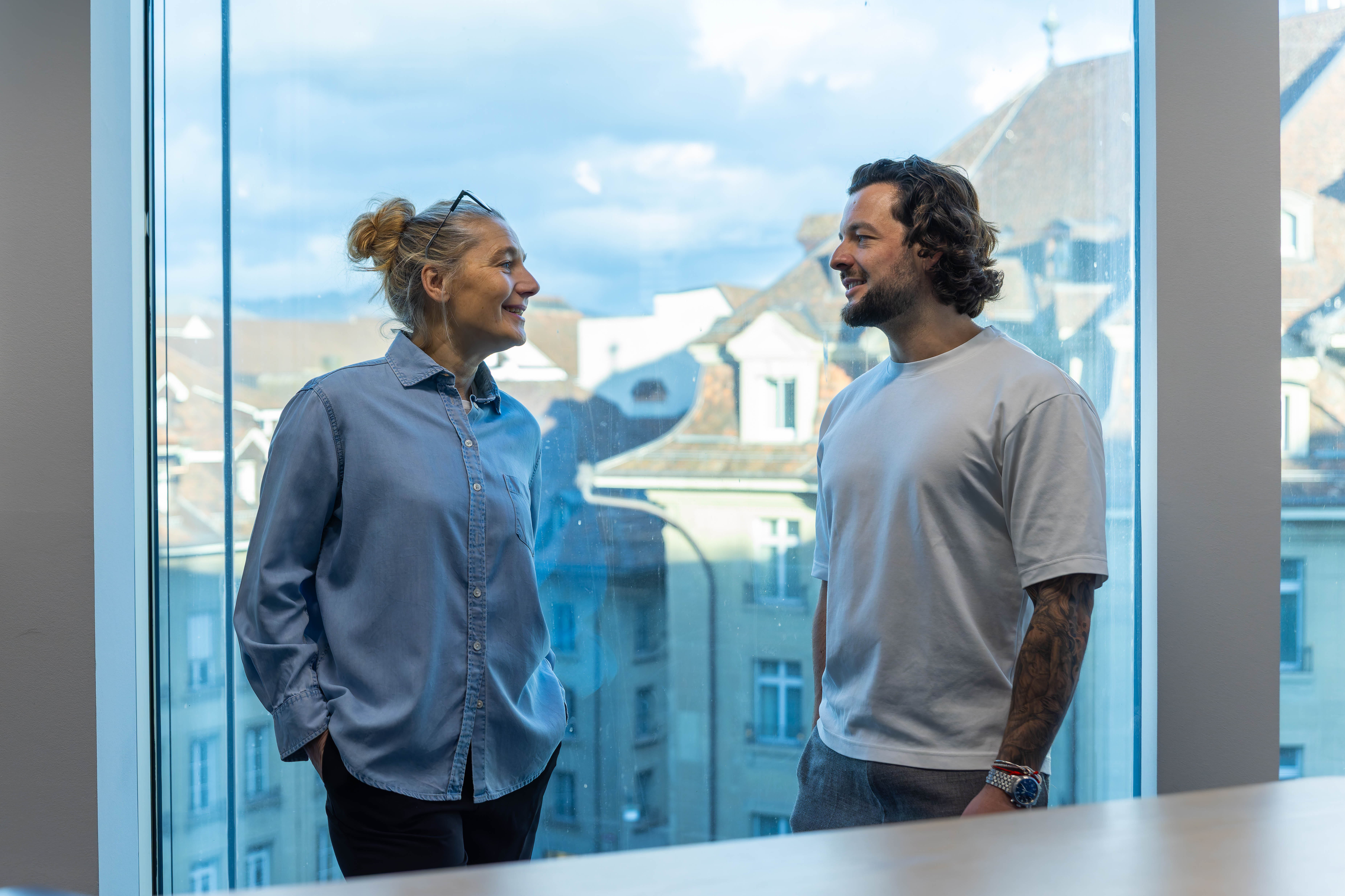 Lachende Business Frau mit lachendem Business Mann vor dem Sitzungsfenster im IT Headhunter Büro von Bornhauser Peoples Management